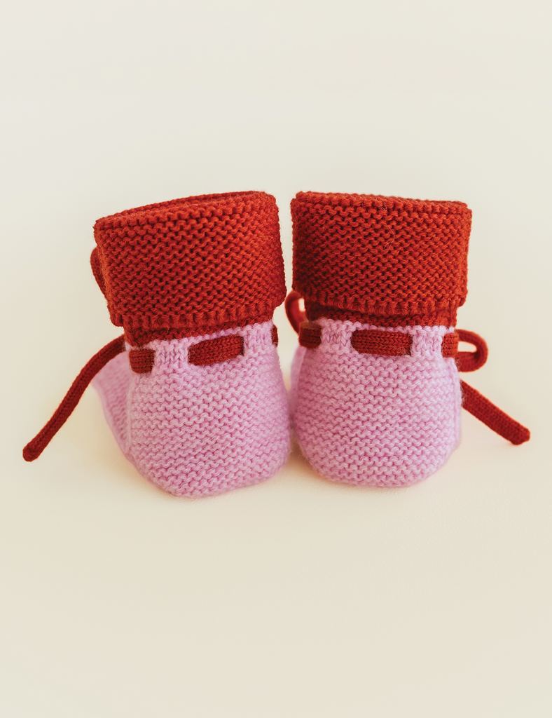 Image of pink and red baby booties on a cream background.