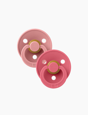 Two pink pacifiers with gold bands on a white background