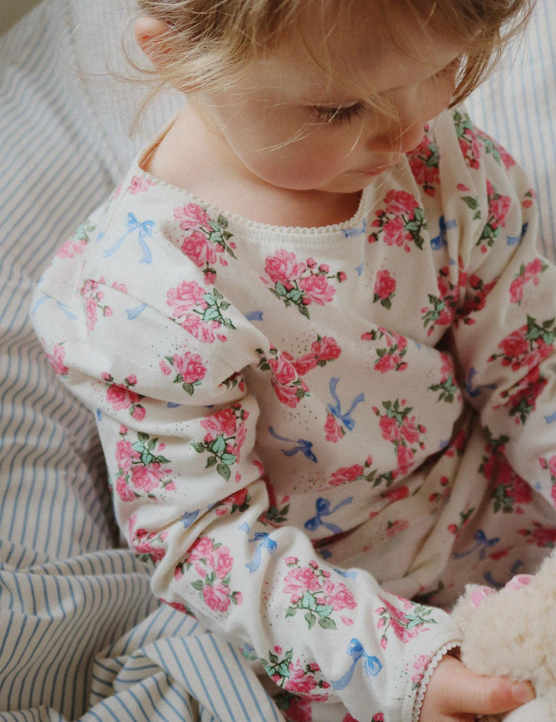 Child wearing a floral long-sleeve shirt sitting on a striped surface.