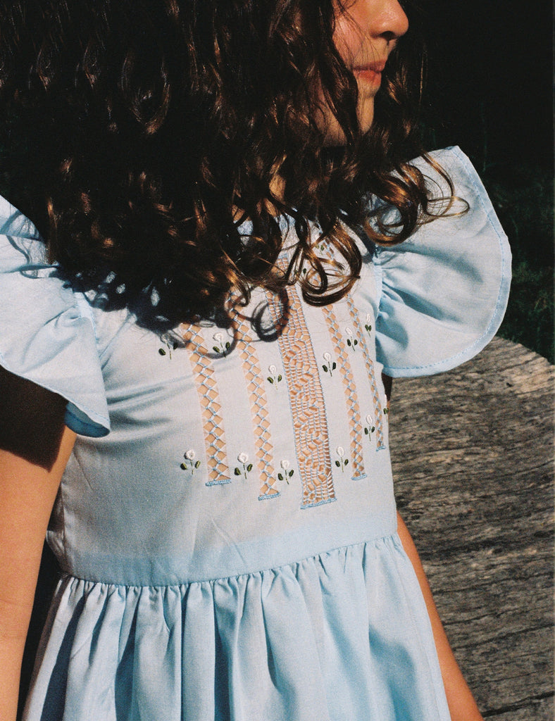 Person wearing a light blue dress with ruffled sleeves and embroidered details.