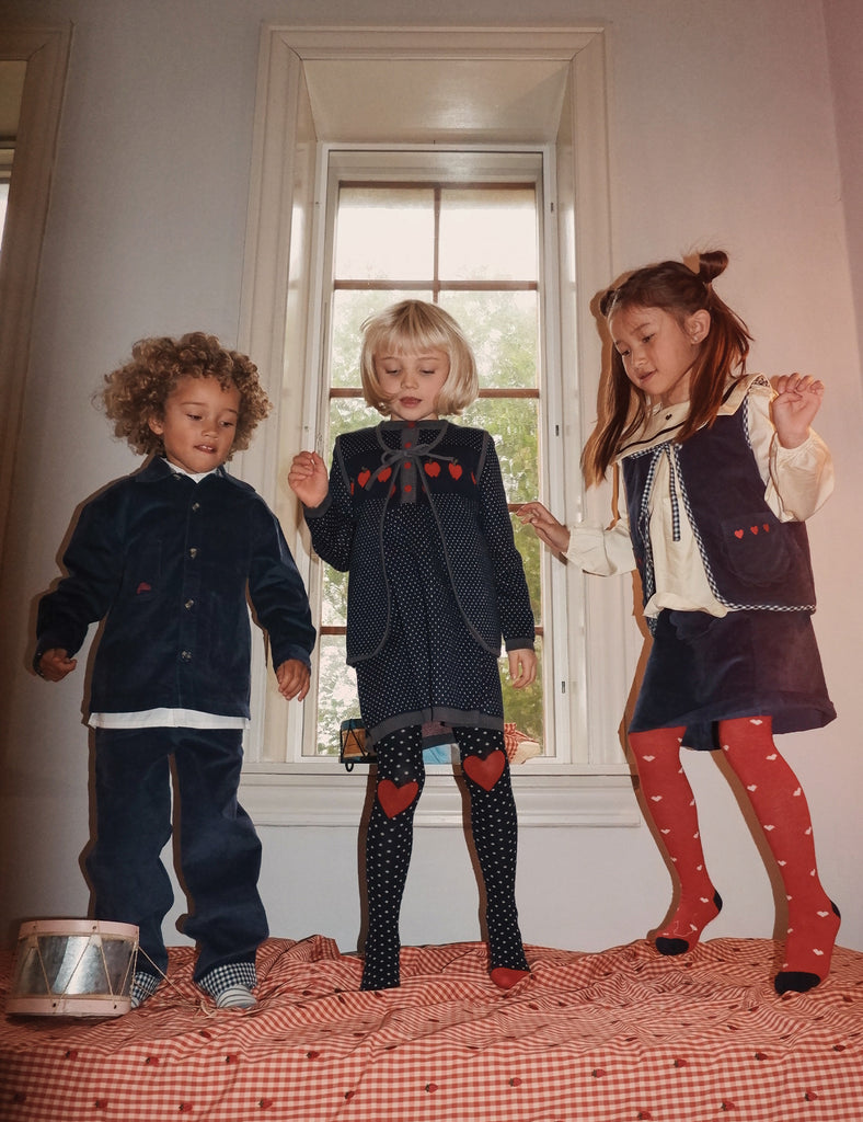 Three children in matching outfits standing in a room with a window in the background.