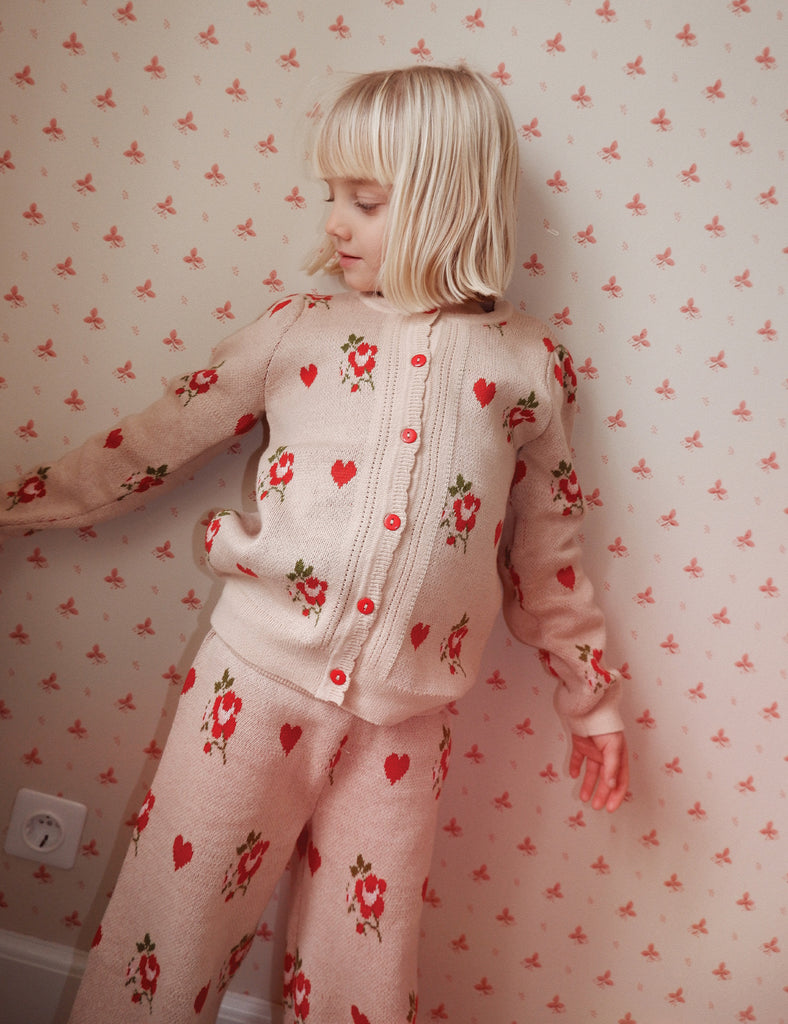 Child wearing a floral outfit standing against a wall with similar floral pattern