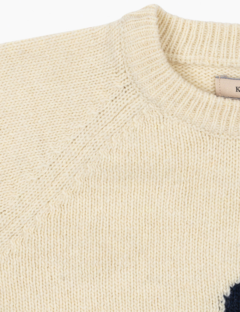 Close-up of a cream-colored knit sweater with a brand label visible.
