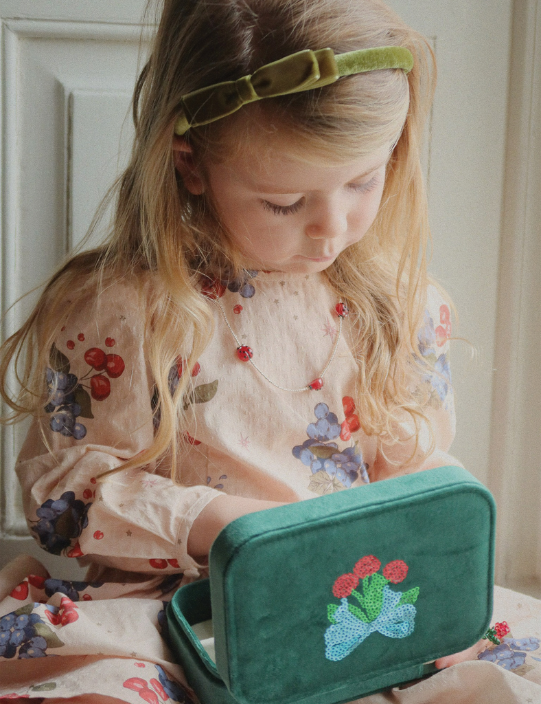 Young girl with a floral dress holding a green embroidered suitcase.