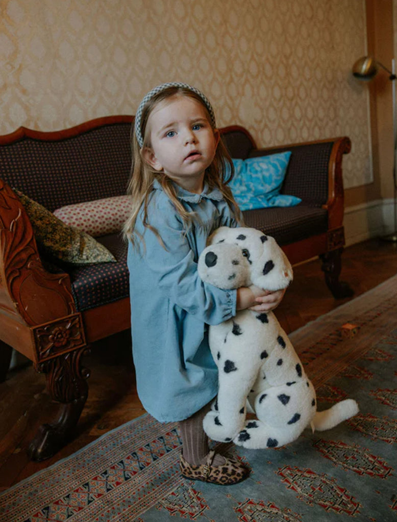 Child holding a stuffed Dalmatian toy in a room with patterned wallpaper and furniture.