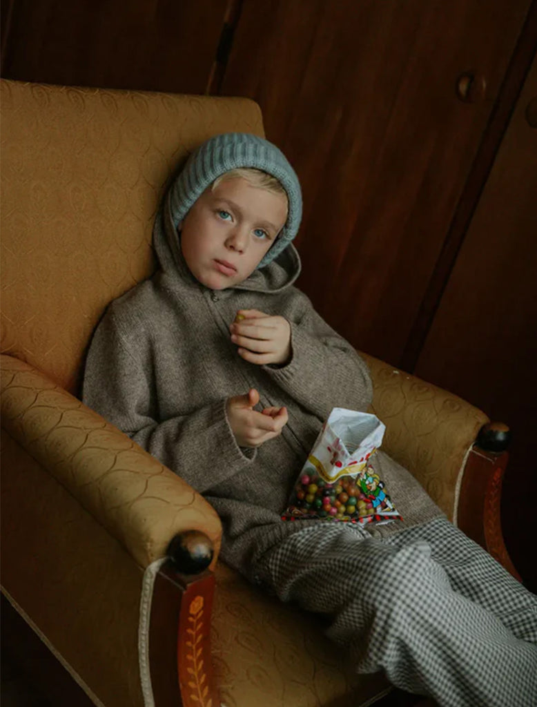 Child sitting on a chair with a bag of candy, wearing a gray outfit and blue hat.