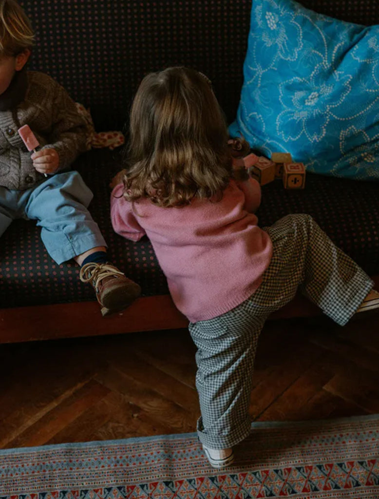 Two children playing on a couch with toys, one child is standing and the other is sitting.