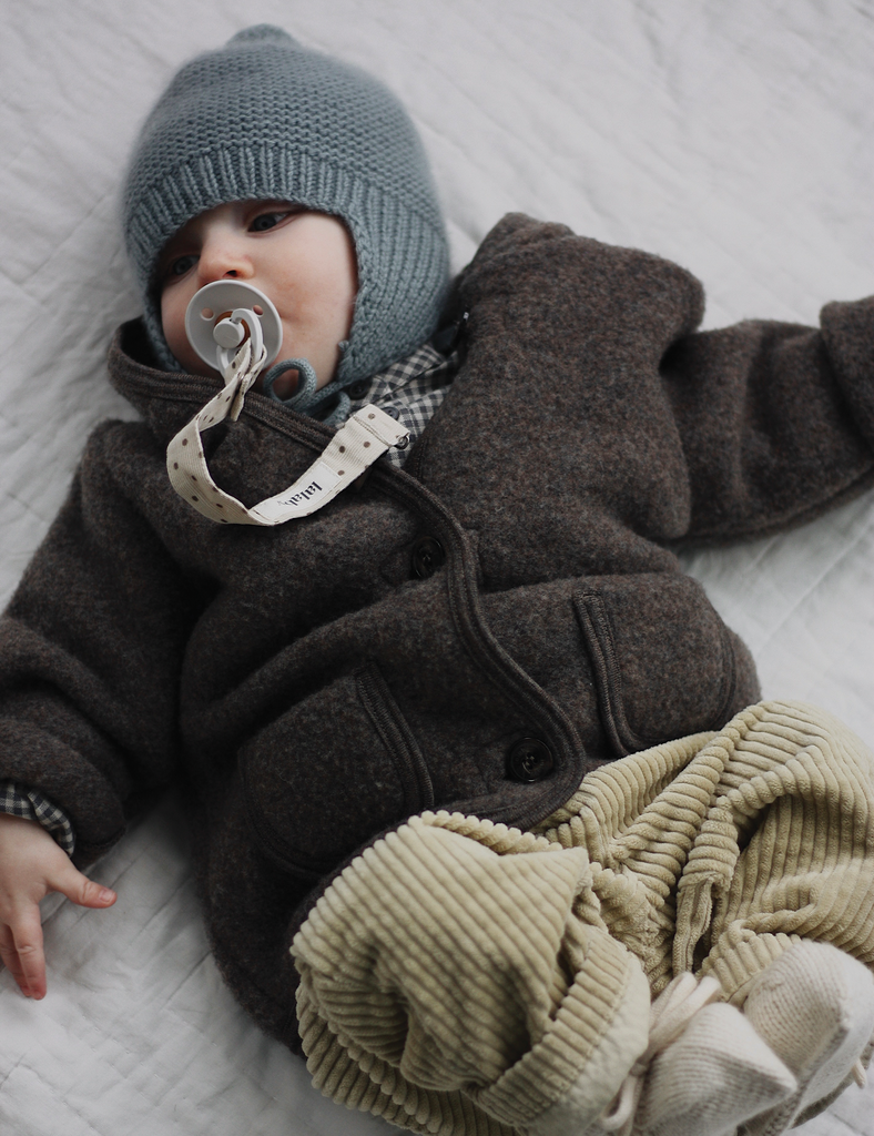 Baby wearing a brown outfit and gray knit hat lying on a textured surface.