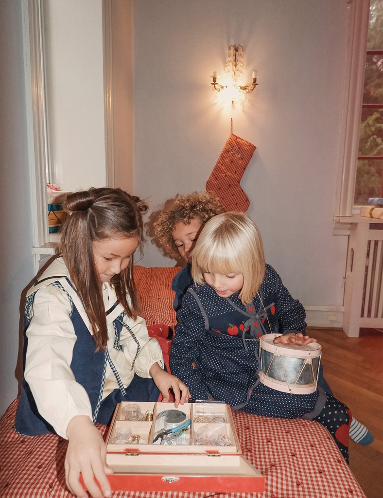 Two children and an adult sitting on a bed looking at a book together, with a Christmas stocking hanging on the wall.