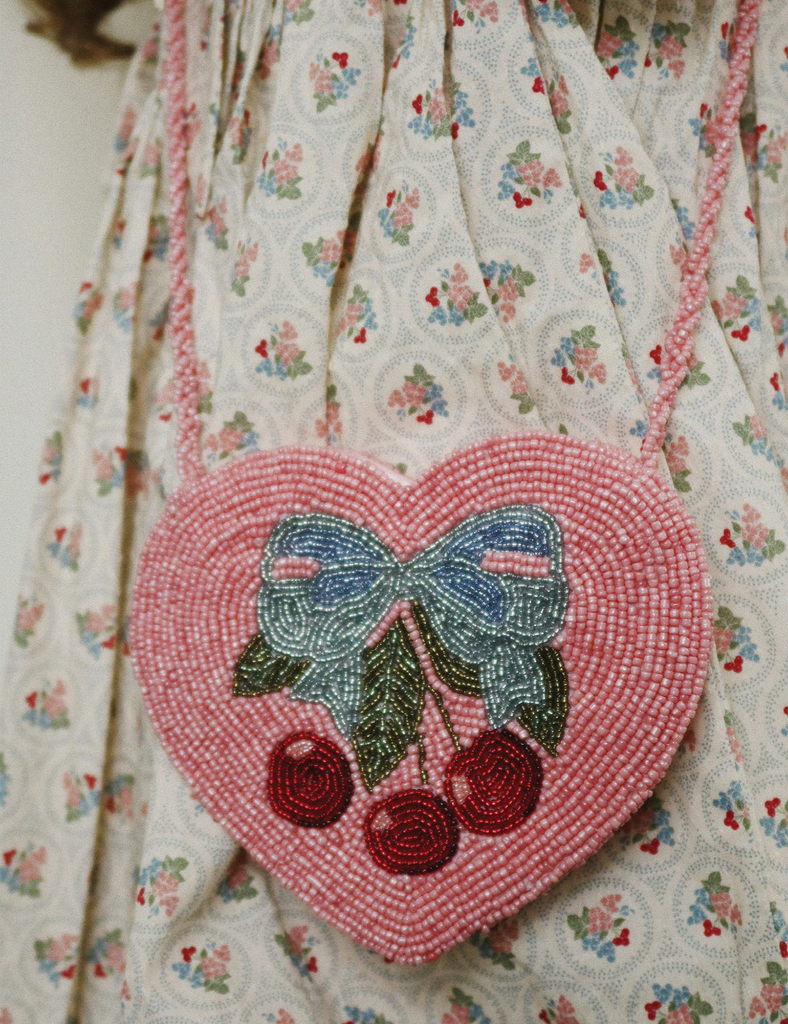 Heart-shaped bag with beaded bow and cherries on a floral background
