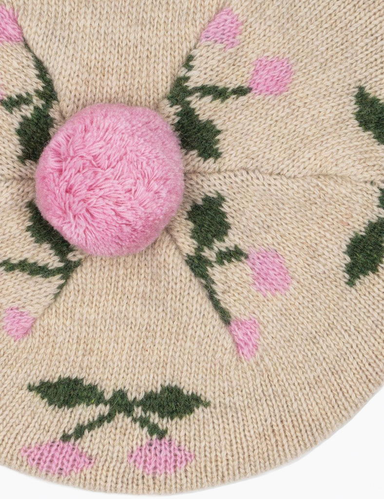 Knitted beret with pink pom-pom and floral pattern on a beige background