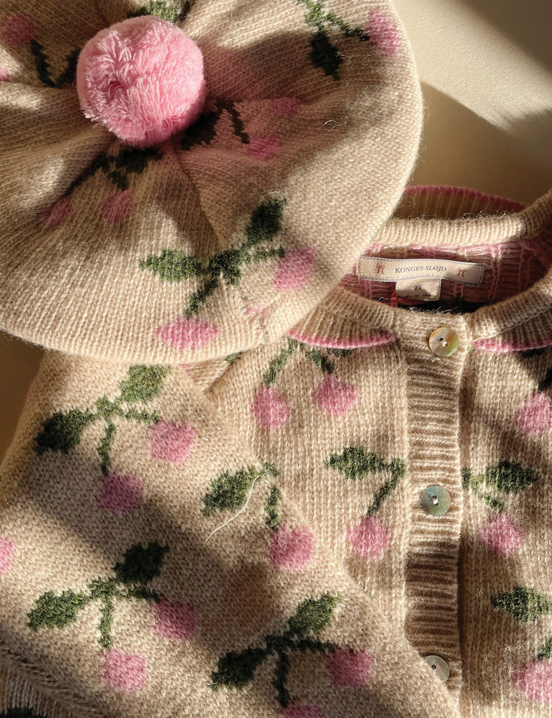 Knitted garment with floral pattern and pink pom-pom on a light background