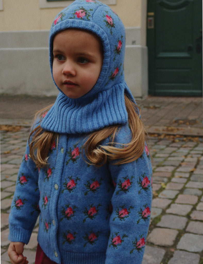 Child wearing a blue floral-patterned coat and hood on a street.