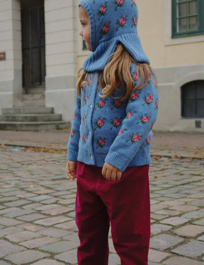 Child wearing a blue floral knitted cardigan and hood in an outdoor setting.