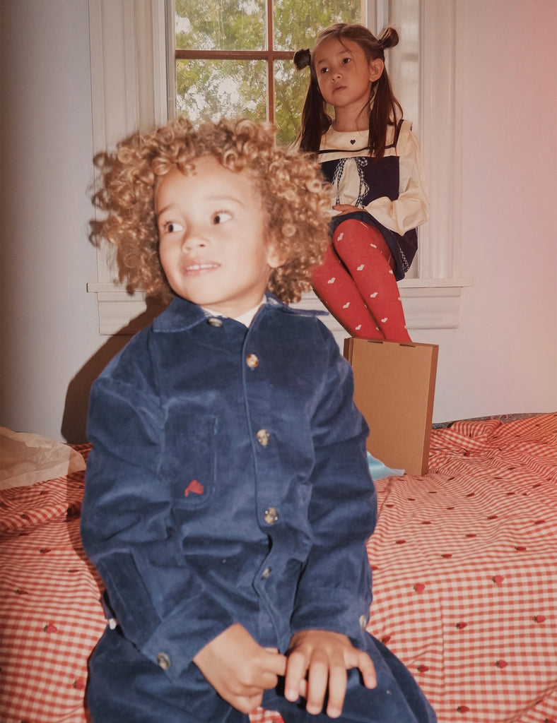 Two children in a room with a checkered bedspread and window.