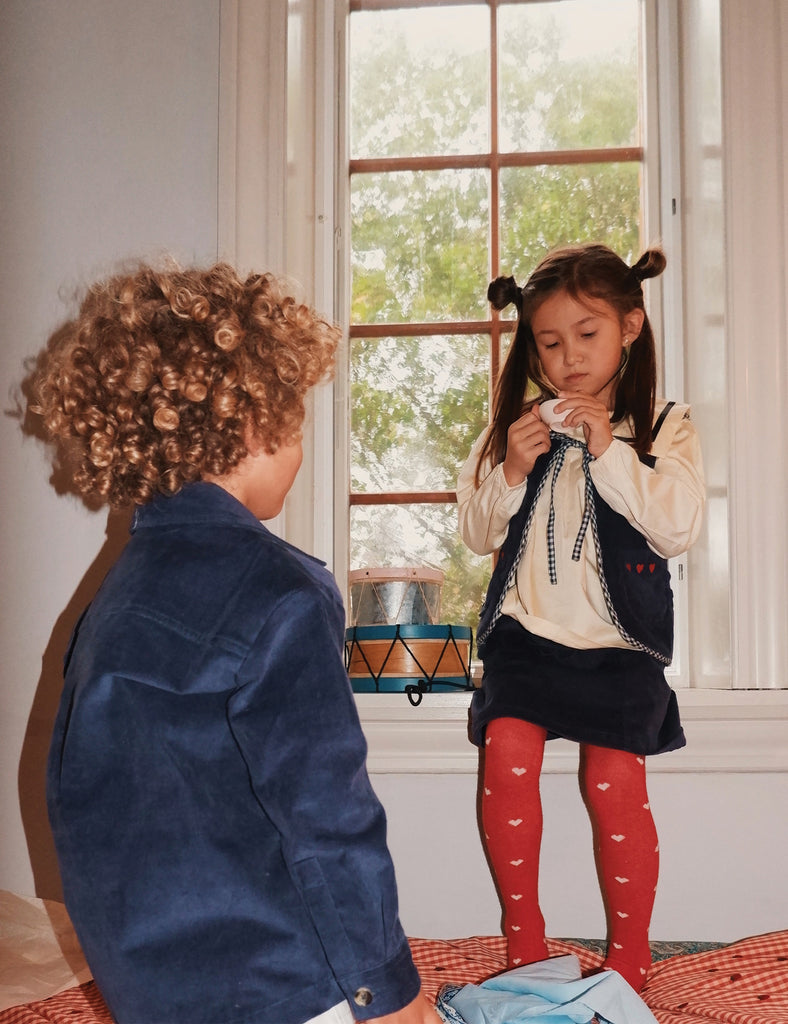 Two children standing in front of a window with a view of trees.