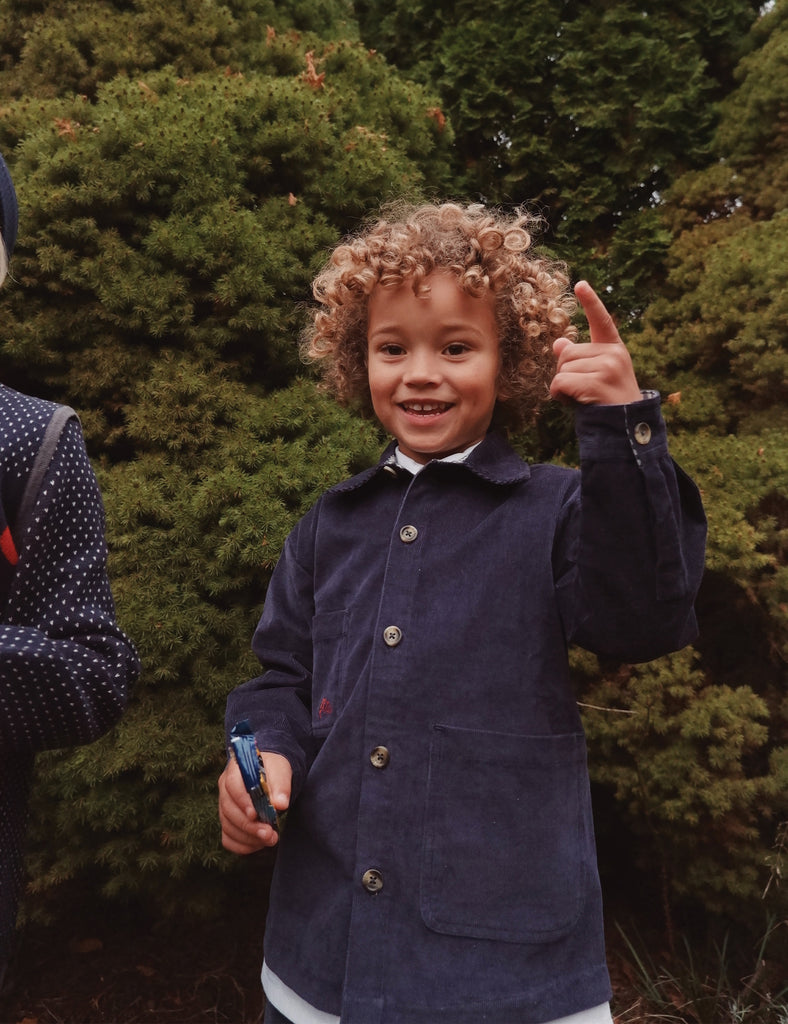 Child in a navy coat standing outdoors with greenery in the background