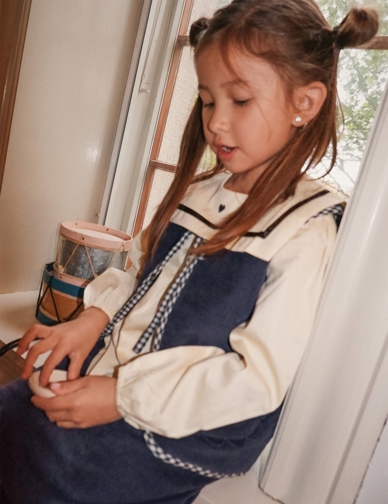 Young girl sitting by a window wearing a navy and white jacket.