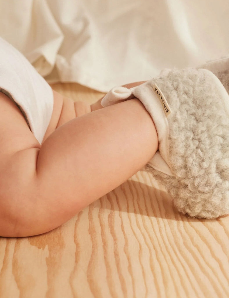 Close-up of a baby's arm wearing a white sock with a textured cuff on a wooden surface.
