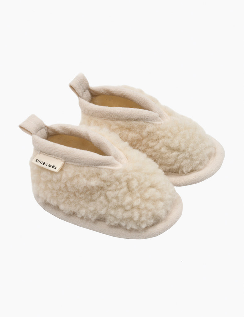 Pair of cream-colored slippers with fuzzy texture on a white background
