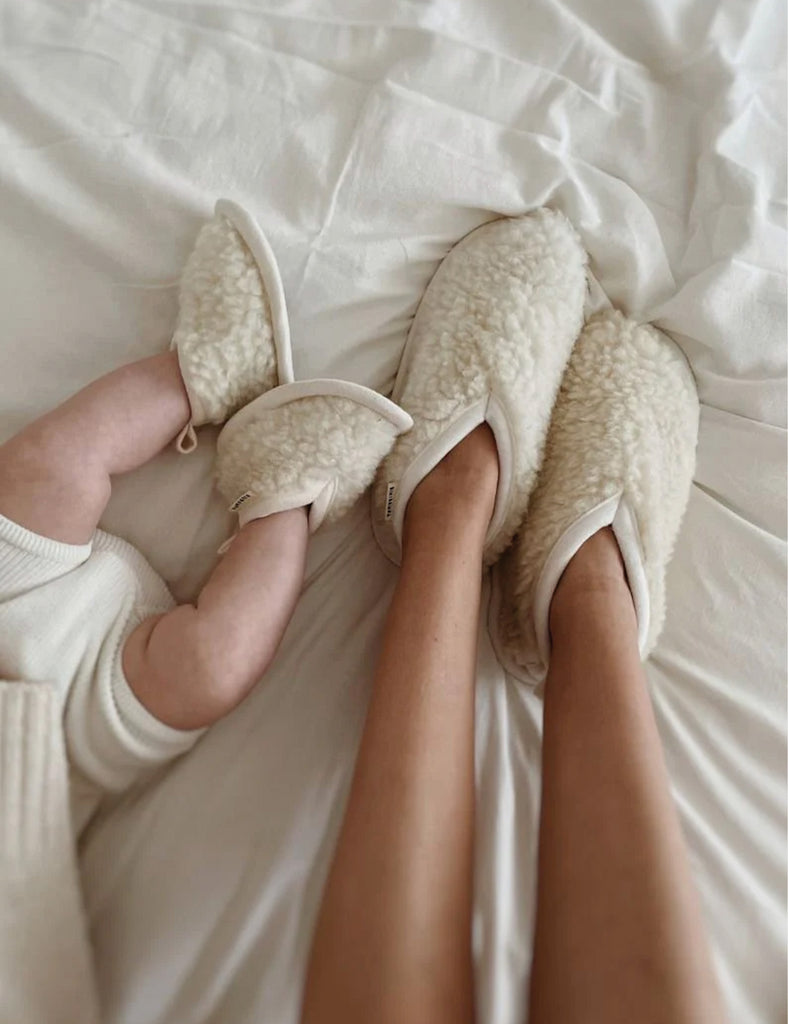 Person wearing fluffy white slippers on a bed