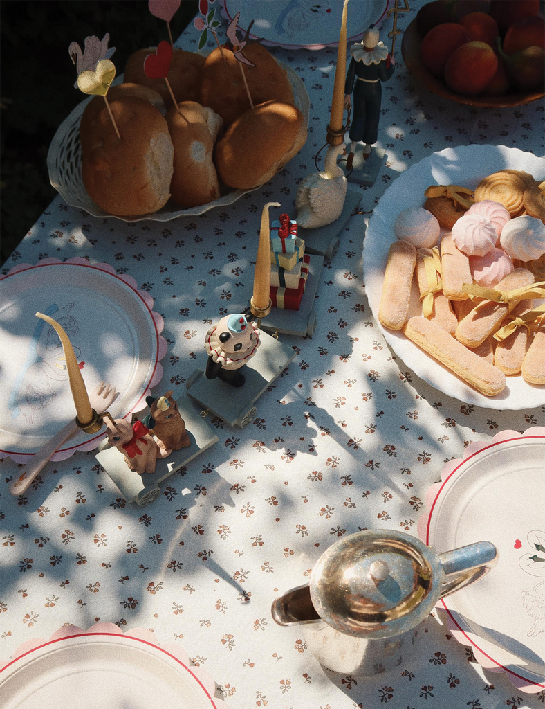 Table setting with miniature food and figures on a patterned tablecloth