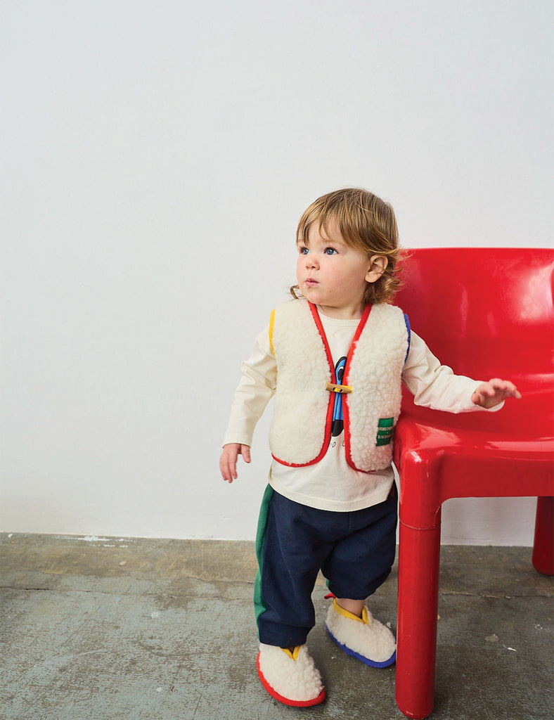 Child standing next to a red chair against a white wall