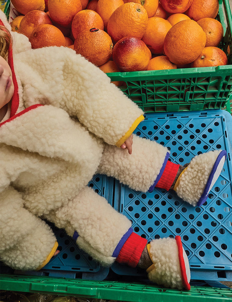 Child in a fluffy outfit lying on a blue plastic crate with oranges in the background