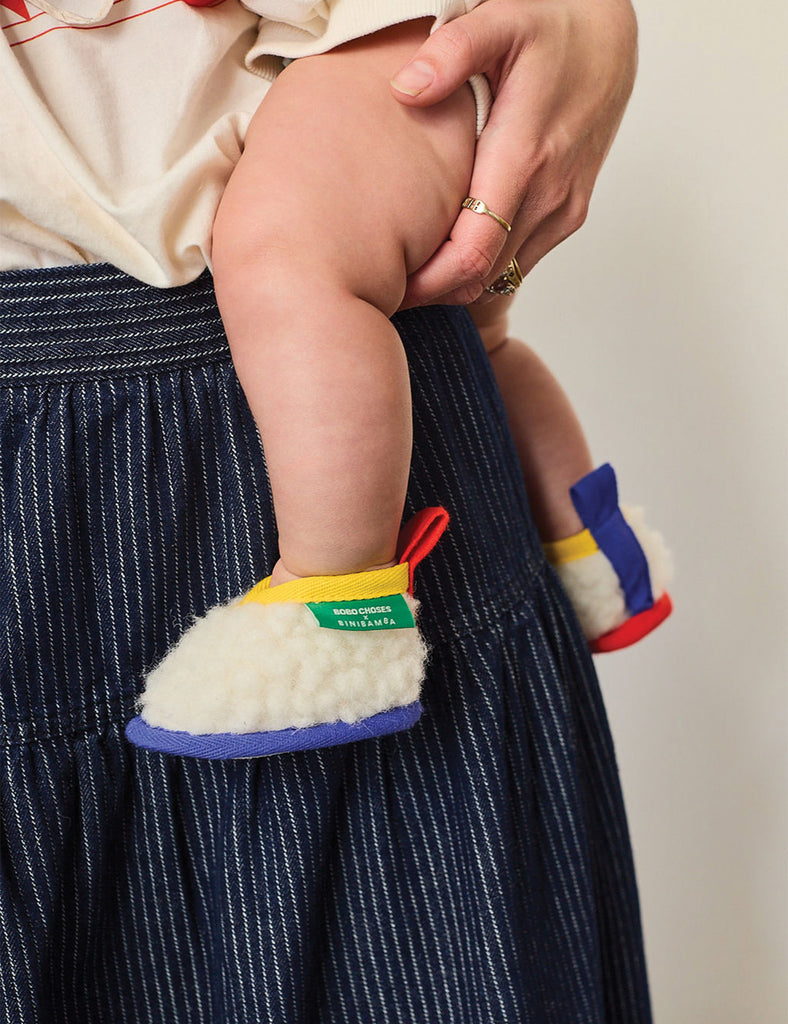 Baby's feet in colorful shoes with a person holding them, wearing a dark blue pinstripe skirt.