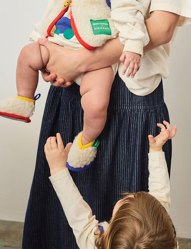 Person holding a child wearing colorful shoes with another child reaching out.
