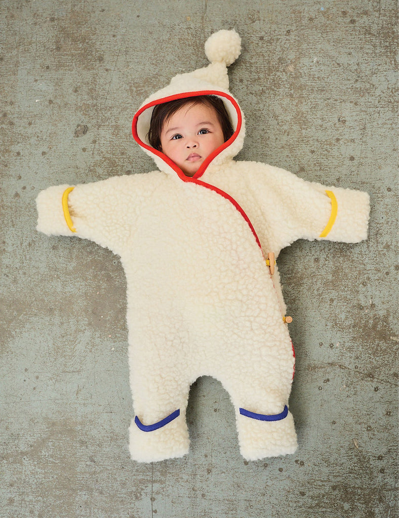 Child wearing a fluffy white onesie with red trim on a textured gray background