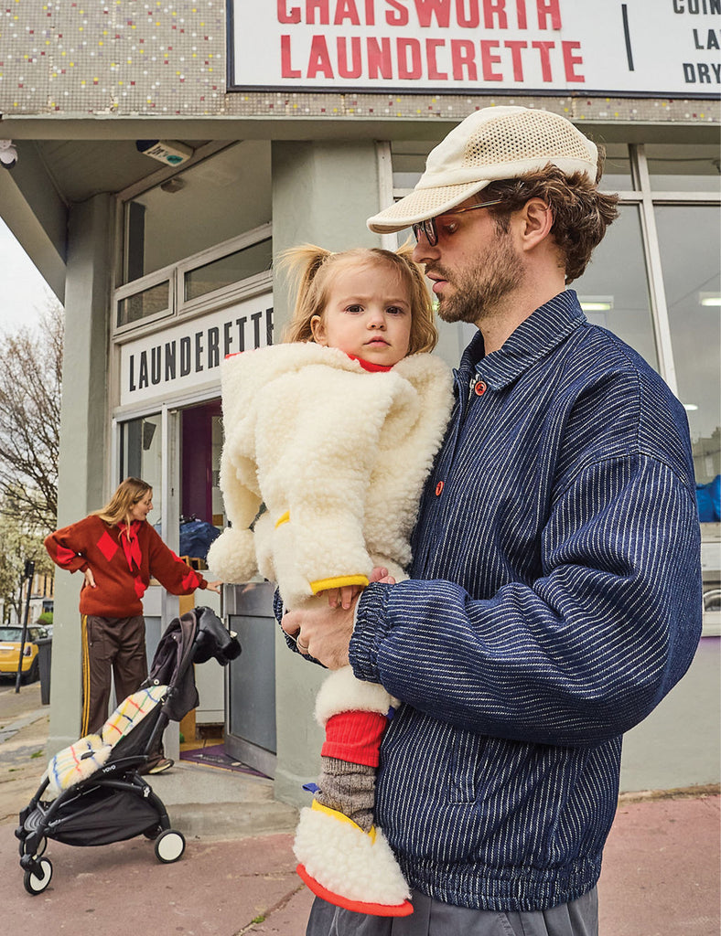 Man holding a child in front of a laundromat with another person in the background.