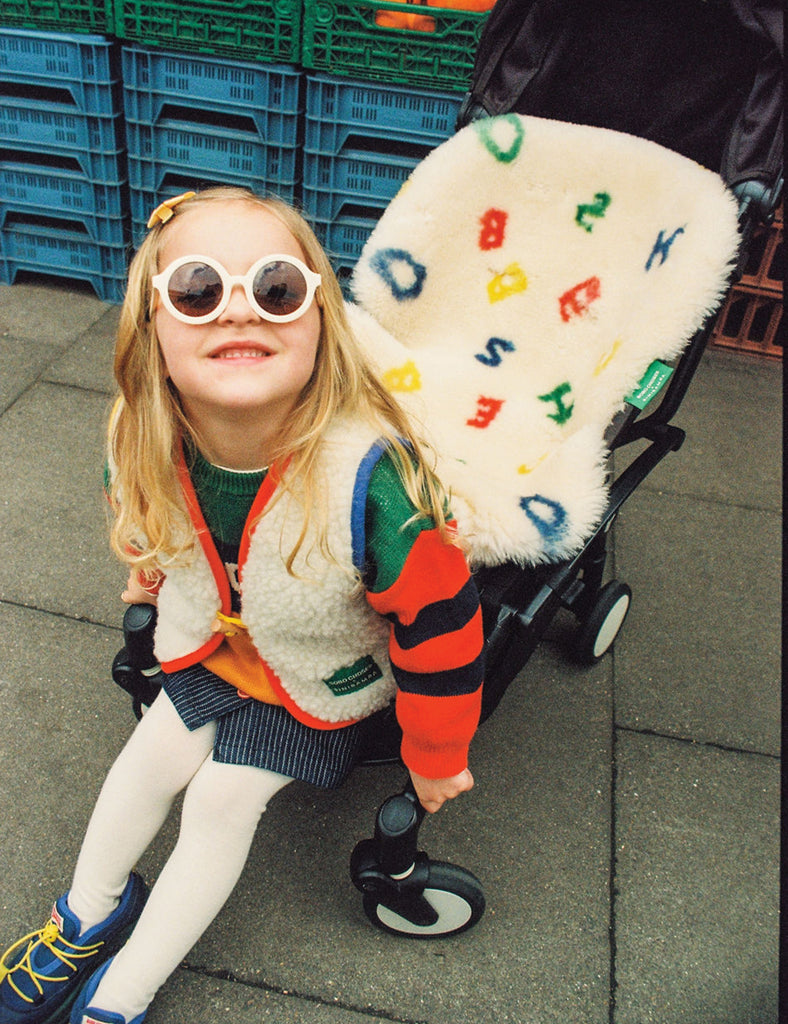 Child in colorful outfit with sunglasses and fluffy toy in stroller