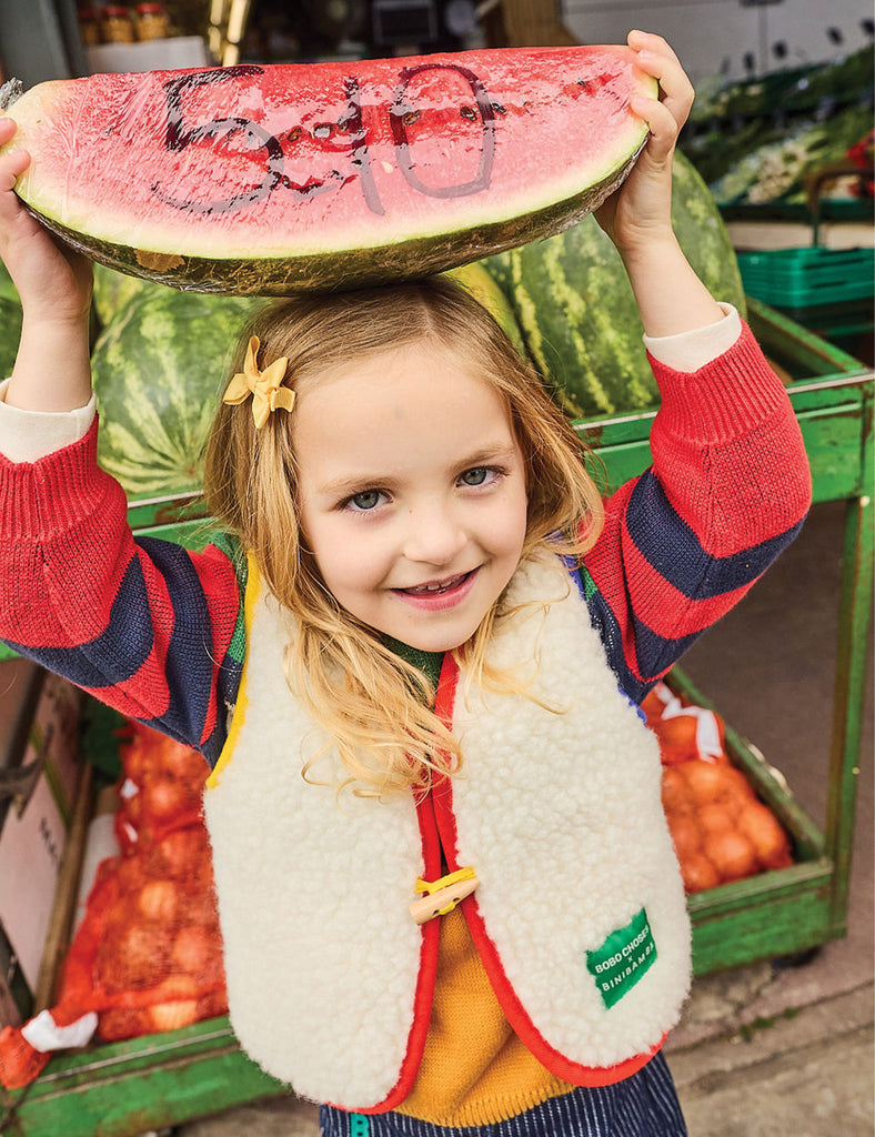 Child holding a watermelon slice with numbers on it in a market setting