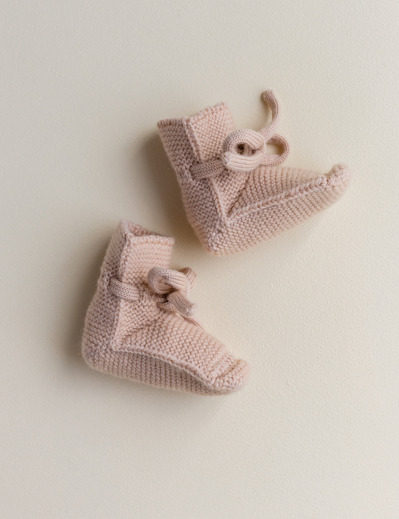 Pair of a light pink beige knit booties on a solid background.