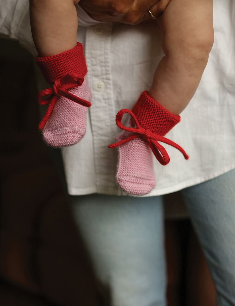 Image of pink and red baby booties on a baby being held.