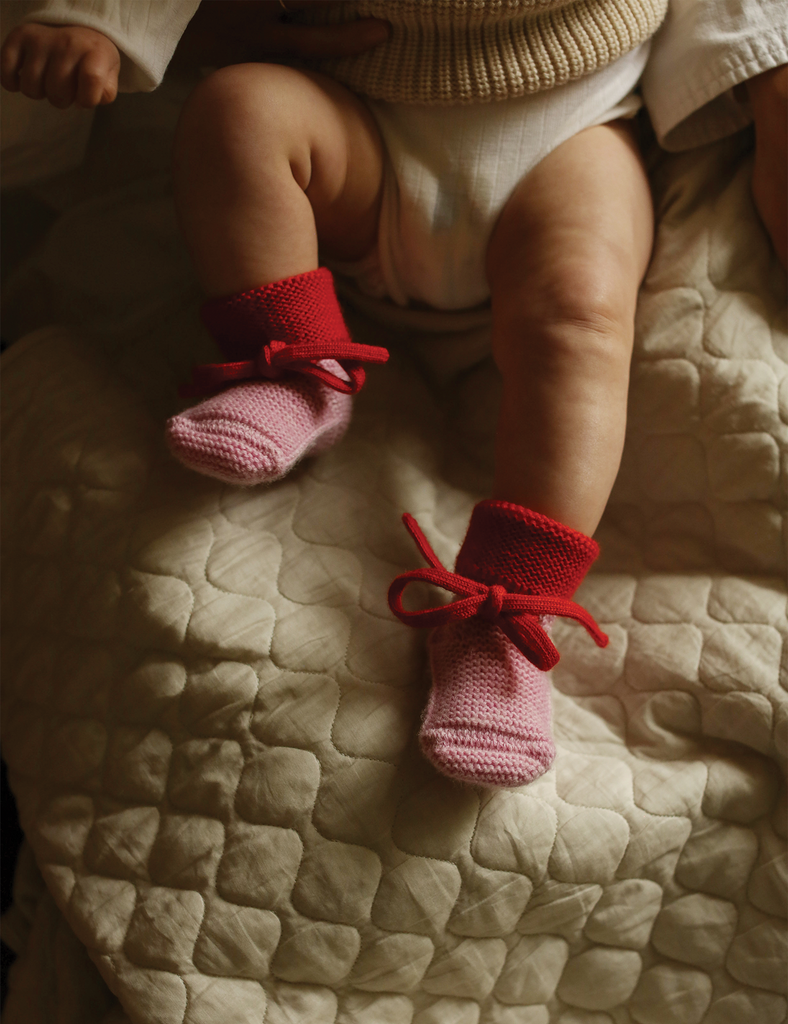 Image of pink and red baby booties on a baby being held.