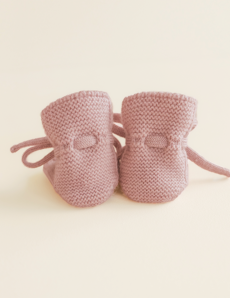Pair of pink knitted baby booties on a light beige background