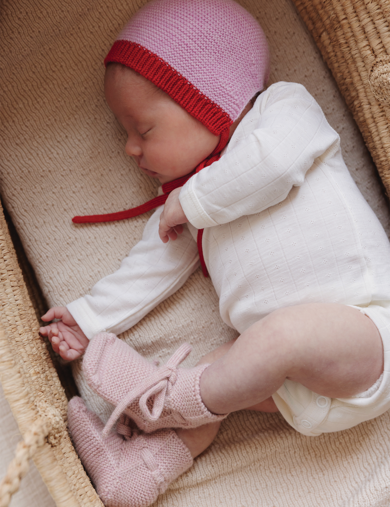 Newborn baby in a pink knitted hat and shoes, sleeping in a basket.