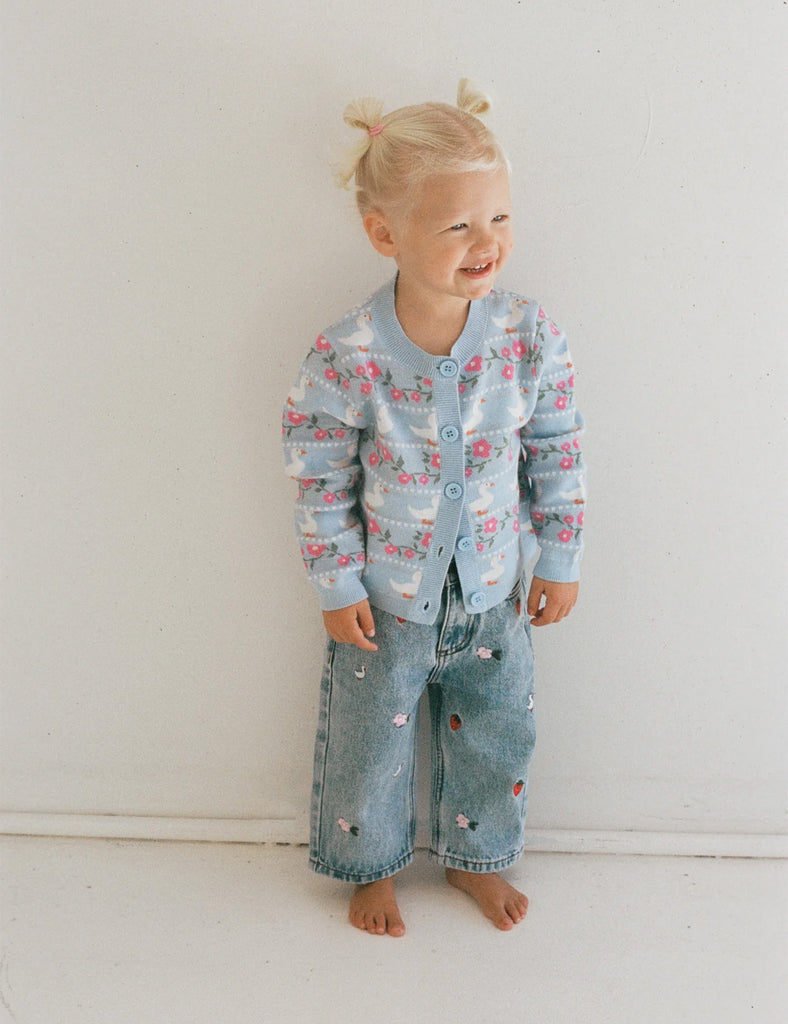 Child wearing a floral shirt and denim pants against a white background