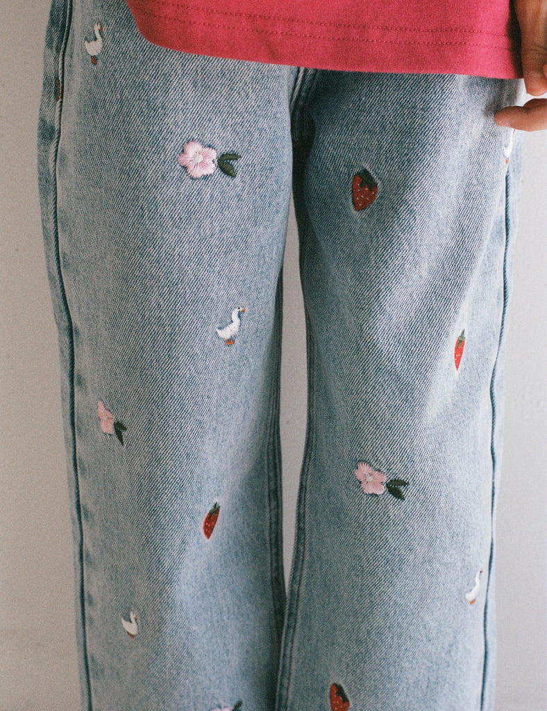 Light blue jeans with floral and heart patterns on a plain background
