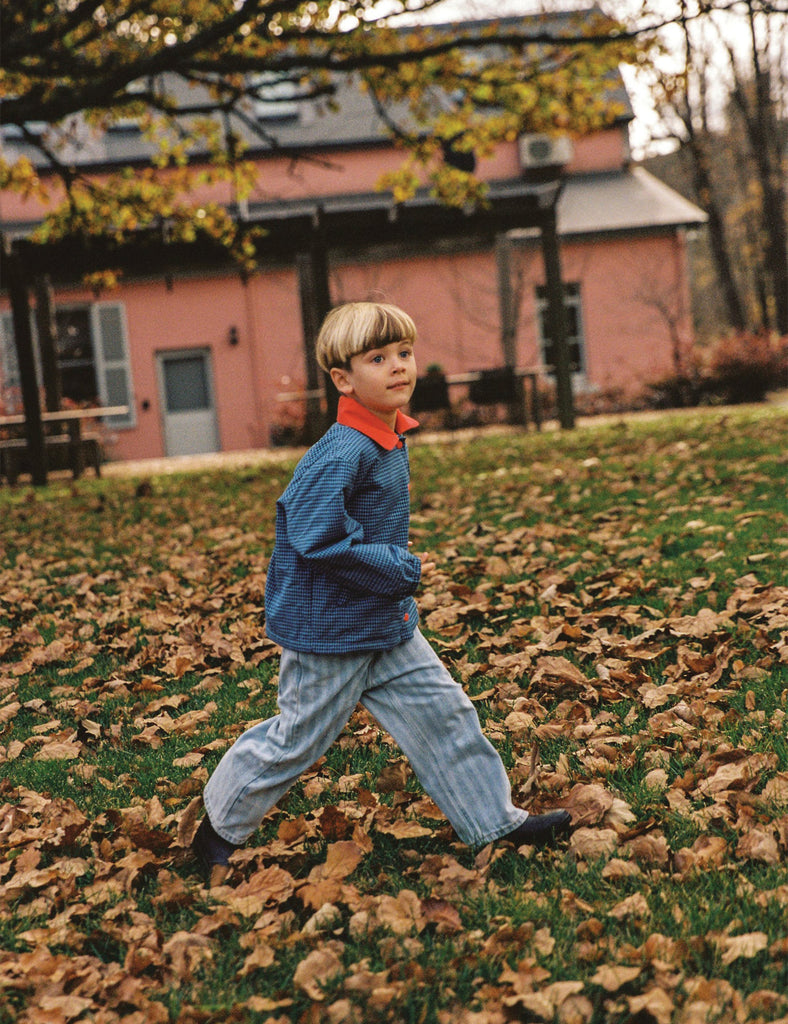 Child walking on a leaf-covered lawn with a pink building in the background