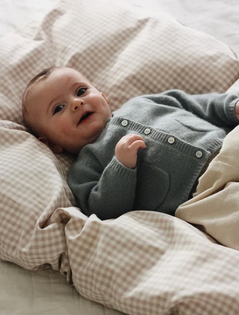 Baby in a gray outfit lying on a checkered blanket