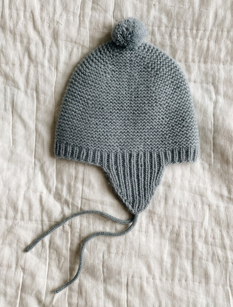 Gray knitted hat with a pom-pom on a beige fabric background