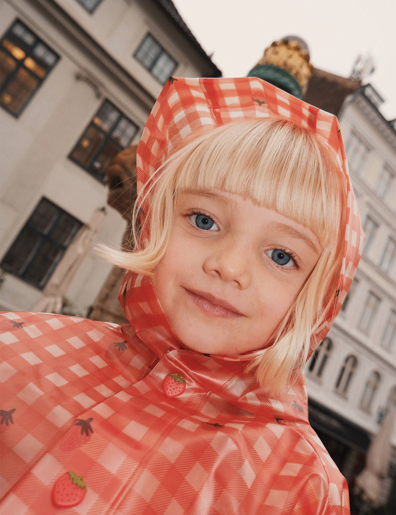 Child wearing a red checkered raincoat with a hood in an urban setting