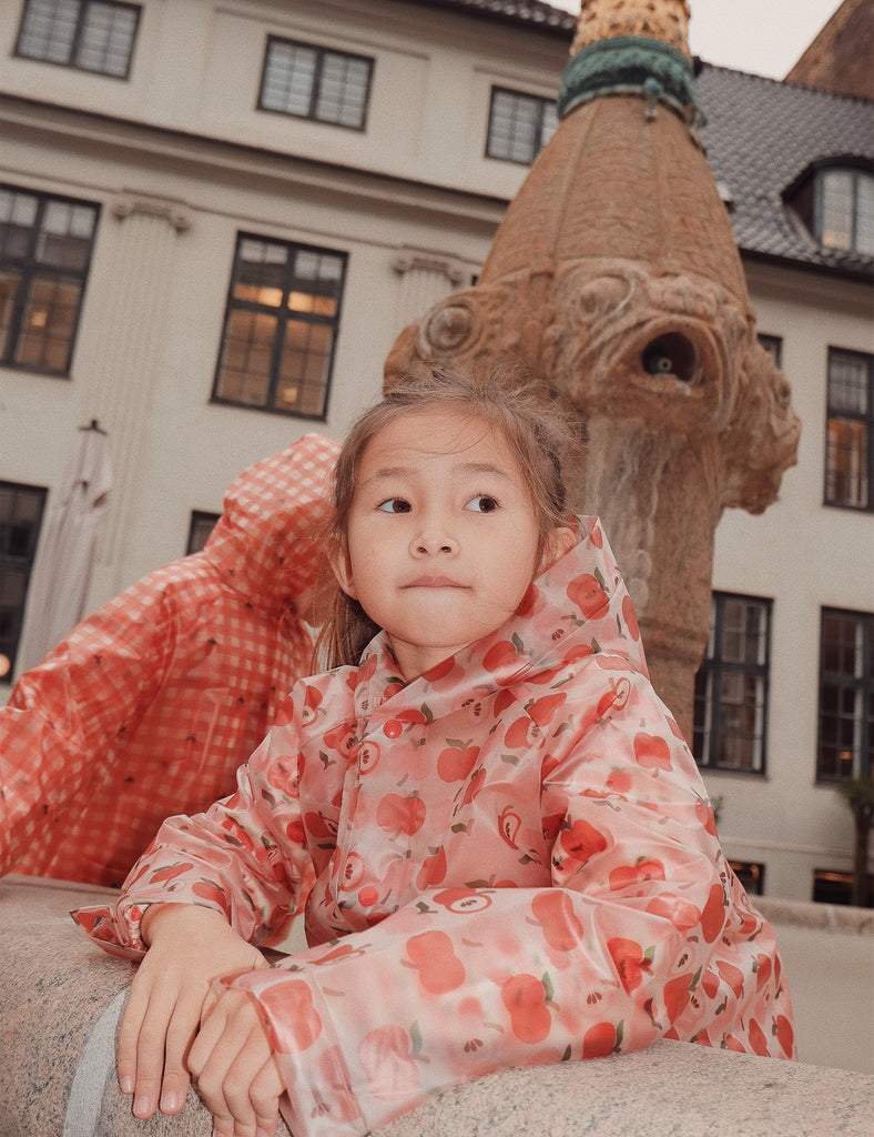 Child in a raincoat sitting on a stone bench with a decorative sculpture in the background.