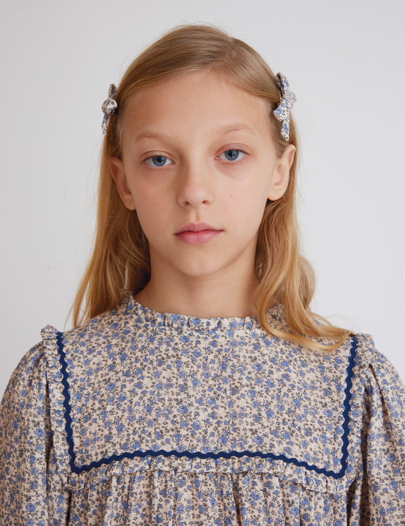 Young girl with floral dress and hair accessories against a plain background
