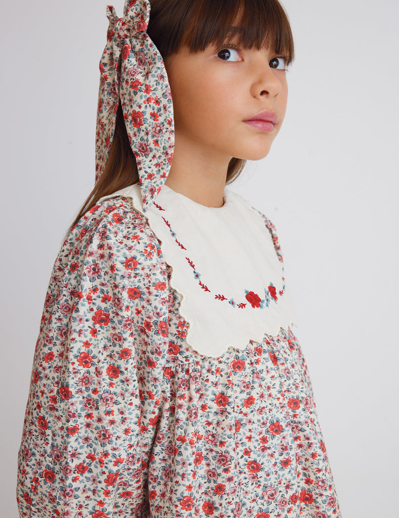 Close up of little girl wearing a floral patterned dress with embroidered roses on the white bib.