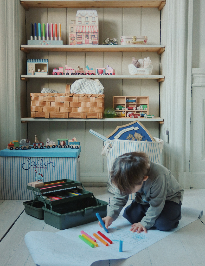 Child playing with toys on a mat in a room with shelves filled with various items.