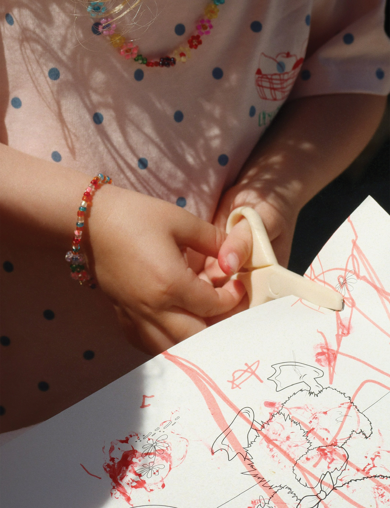 Child's hands holding a small object with colorful bracelet, on a surface with red and black drawings.